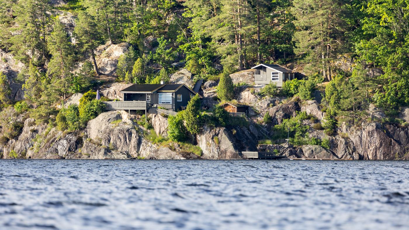 Wooden cabins tucked into a pine-covered rocky shoreline above a still lake